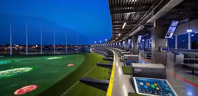 Topgolf multi-level range at night, illuminated hitting bays and glowing targets.