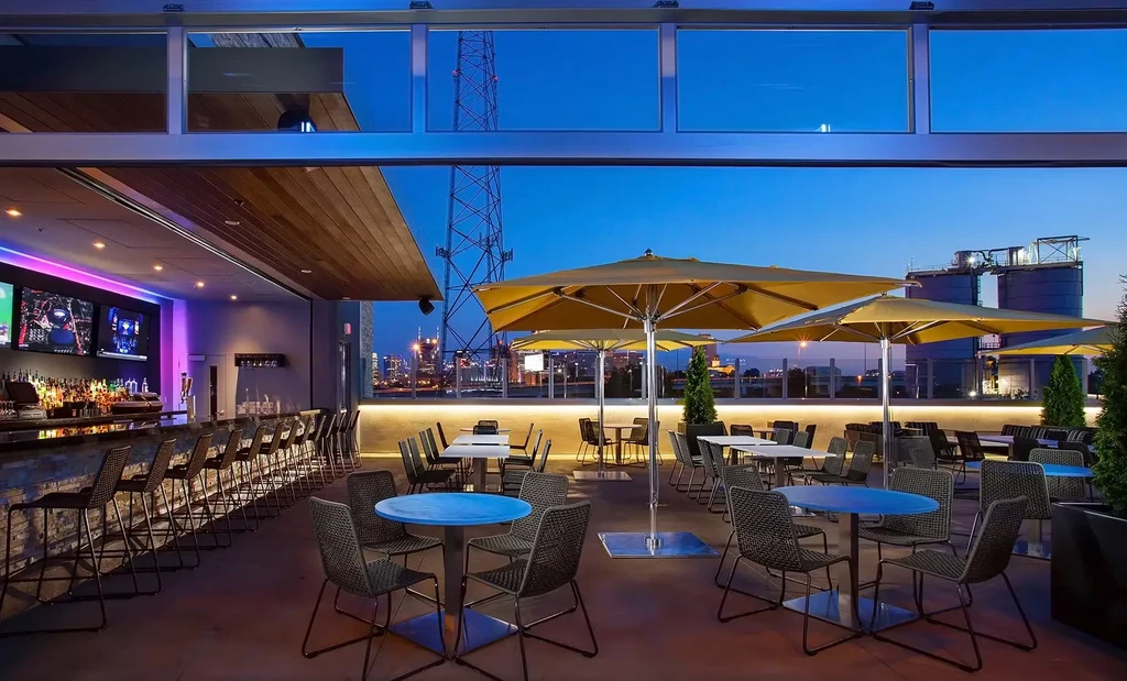 Empty modern rooftop bar and patio overlooking a city skyline.