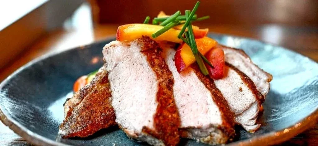 Gourmet roasted meat slices with peaches and chives on a dark plate.