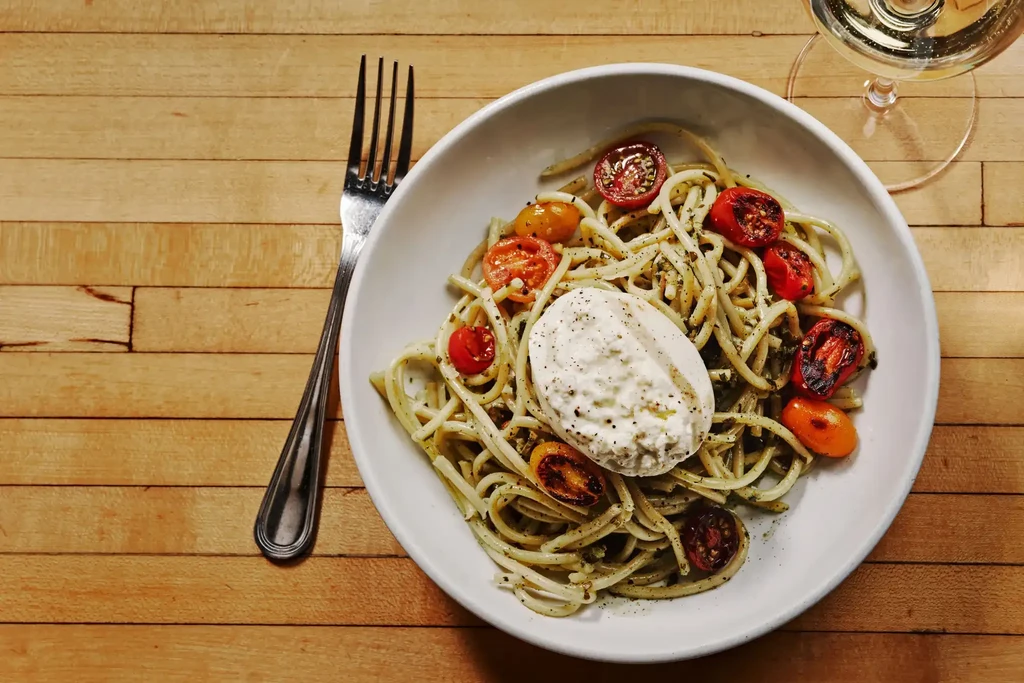 Close-up of bucatini pasta with pesto, roasted tomatoes, and ricotta cheese.