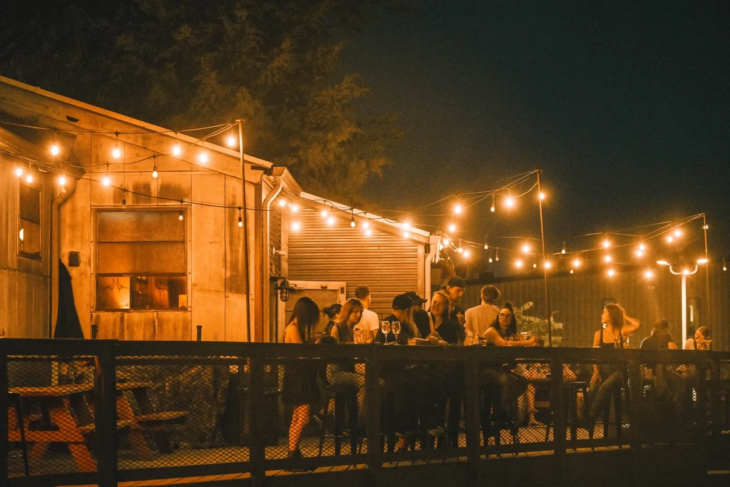 Nighttime outdoor social gathering with people under festive string lights.