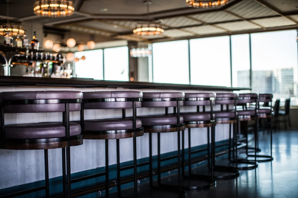 Empty dark bar stools line a modern bar with city views.