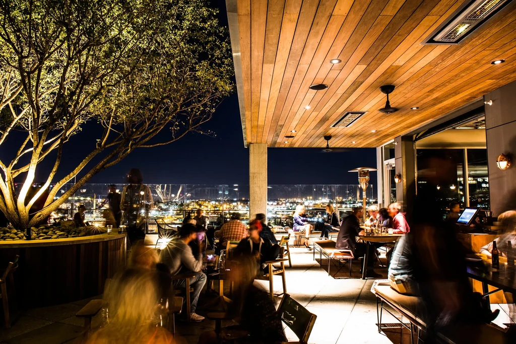 Lively nighttime rooftop bar overlooking a city skyline.