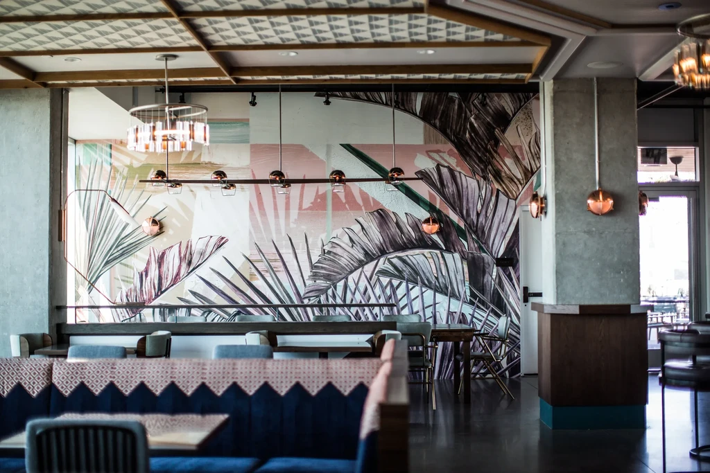 Modern restaurant interior: colorful tropical mural, bar, and blue booths.