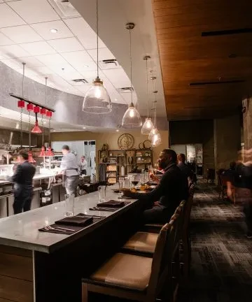 Modern restaurant interior: open kitchen, bar, and patrons with drinks.
