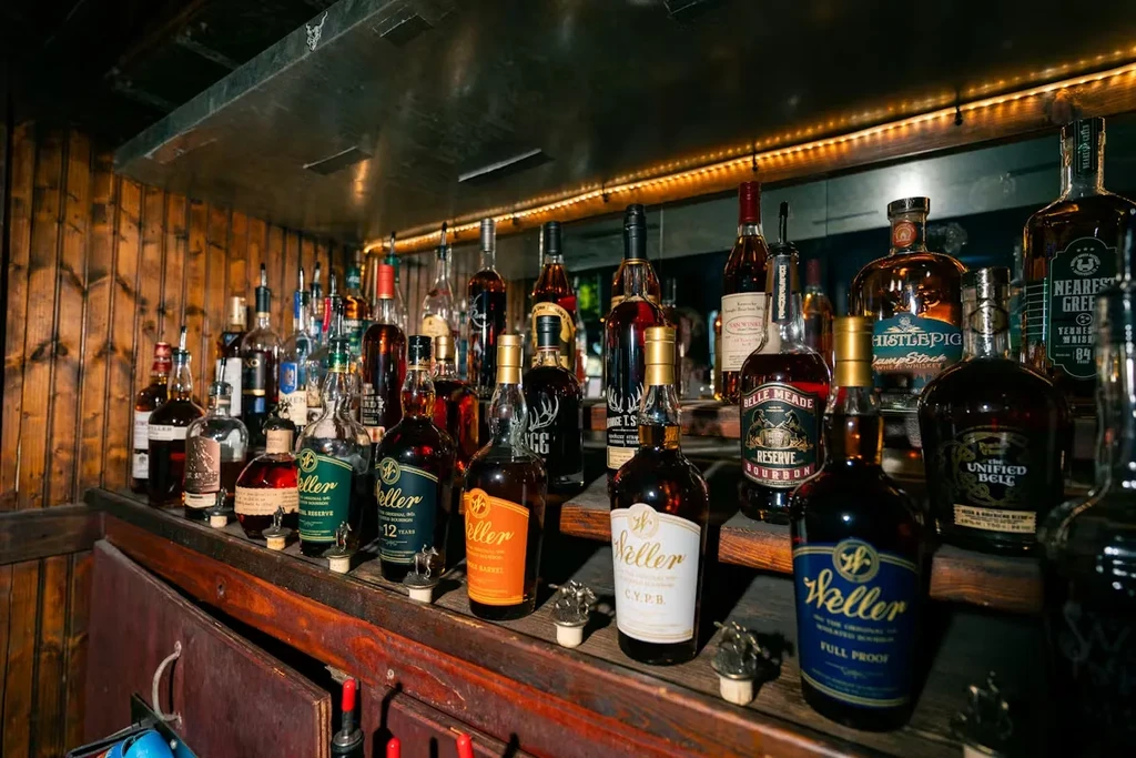 Numerous whiskey and bourbon bottles arranged on a tiered bar shelf.