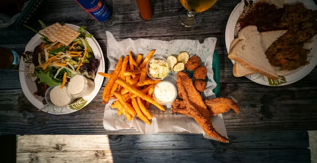 Rustic table with fried fish, fries, salad, stew, and drinks.