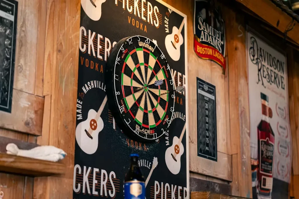 Dartboard with three darts on a wooden wall, surrounded by bar signs.