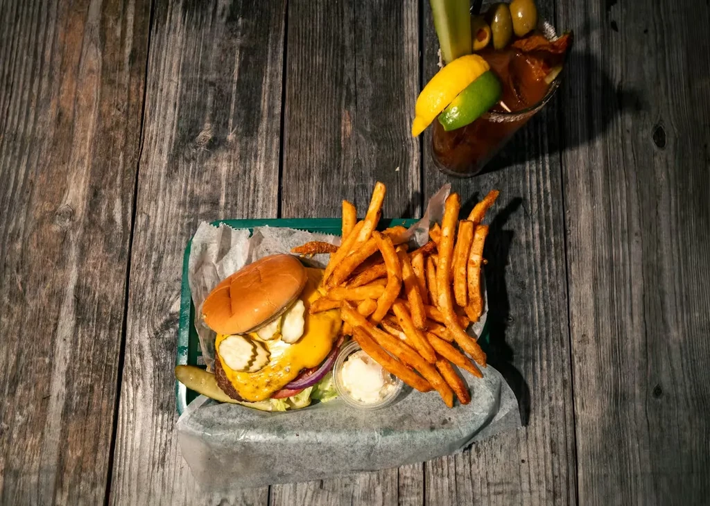 Cheeseburger, fries, and garnished Bloody Mary on rustic wooden table.