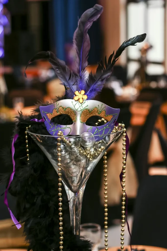 Silver and purple masquerade mask centerpiece with feathers and gold beads.