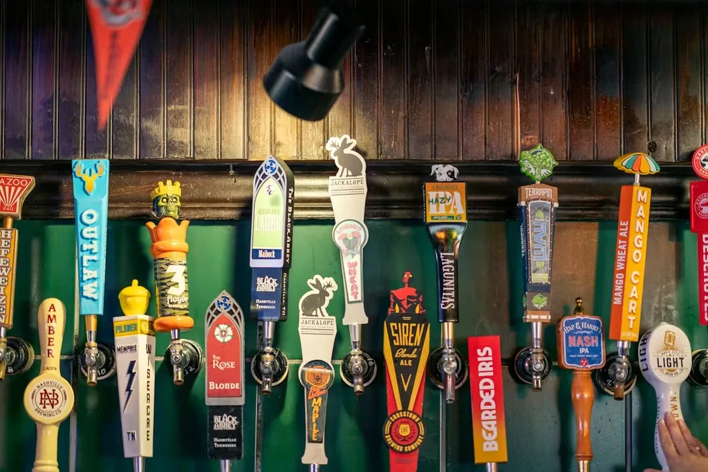 Seventeen uniquely designed beer tap handles with distinct shapes and a hand.