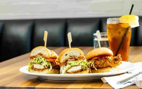 Three breaded chicken sliders with iced tea on a restaurant table.