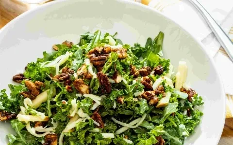 Overhead green kale salad with candied nuts, cheese, and apple slices.