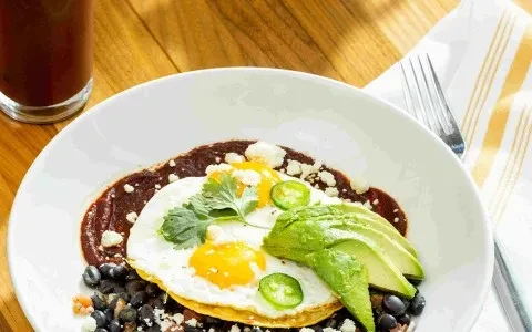 Colorful fried eggs, black beans, avocado, and garnishes, top-down view.