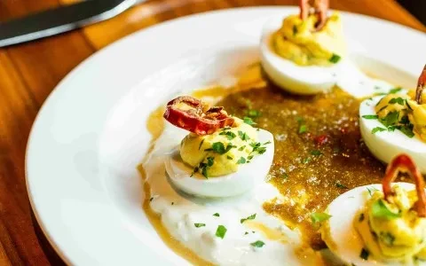 Close-up of deviled eggs with herbs, red pepper, and two sauces.
