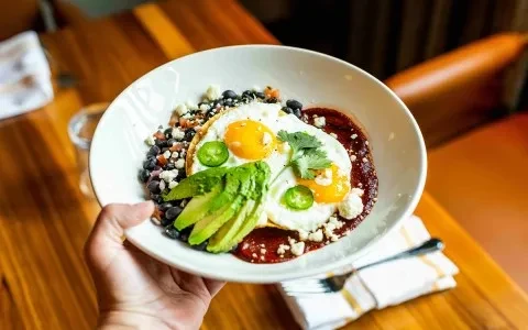 Hand holding vibrant breakfast bowl with sunny-side-up eggs, beans, avocado.