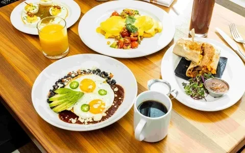 Vibrant breakfast spread: deviled eggs, Eggs Benedict, burritos on a wood table.