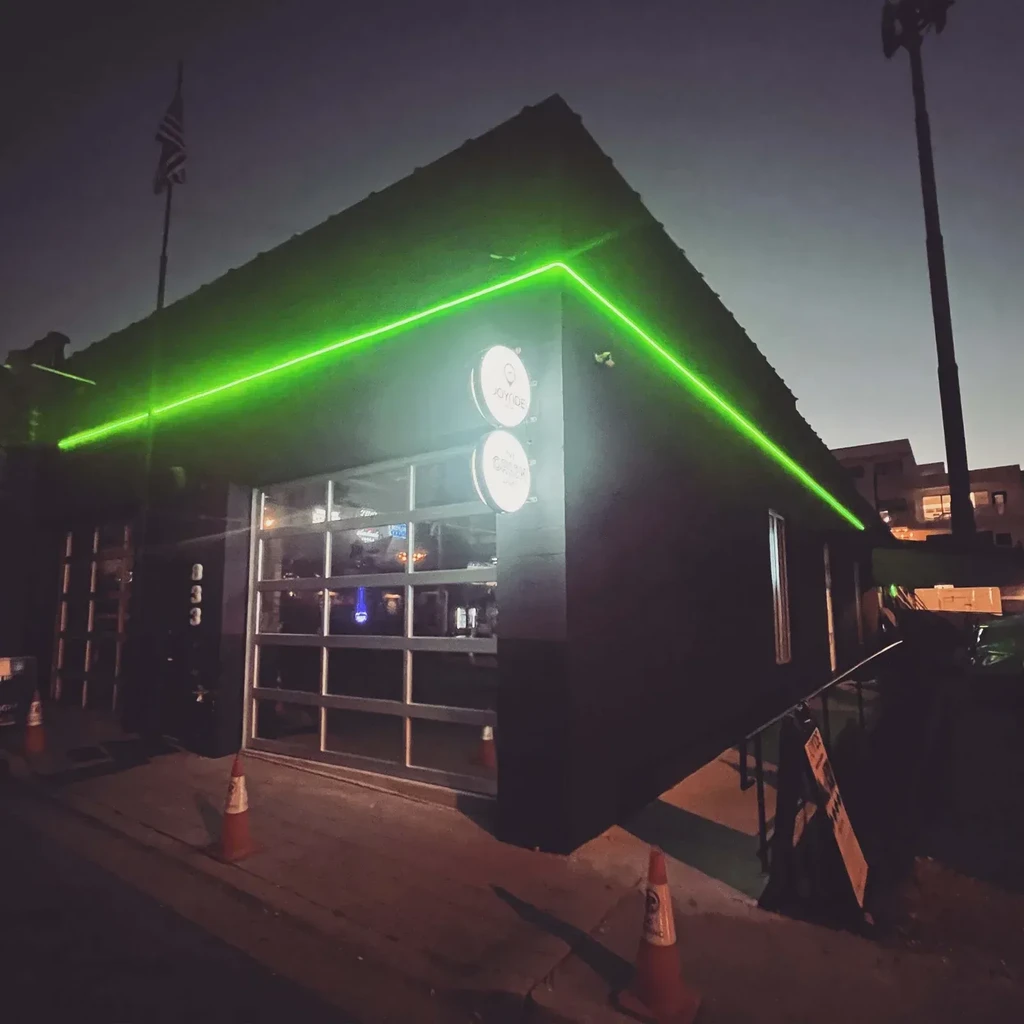 Dark building with green neon roof light, 'JOYRIDE THE GRIND' signs.