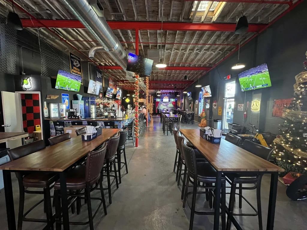 Industrial sports bar with communal tables, multiple TVs, and Christmas tree.