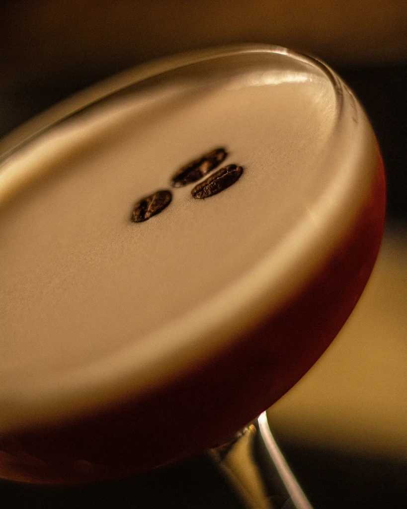 Close-up of an espresso martini with creamy foam and three coffee beans.