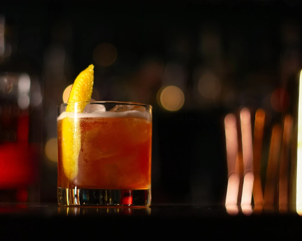 Cold reddish-orange cocktail with citrus peel in a rocks glass.