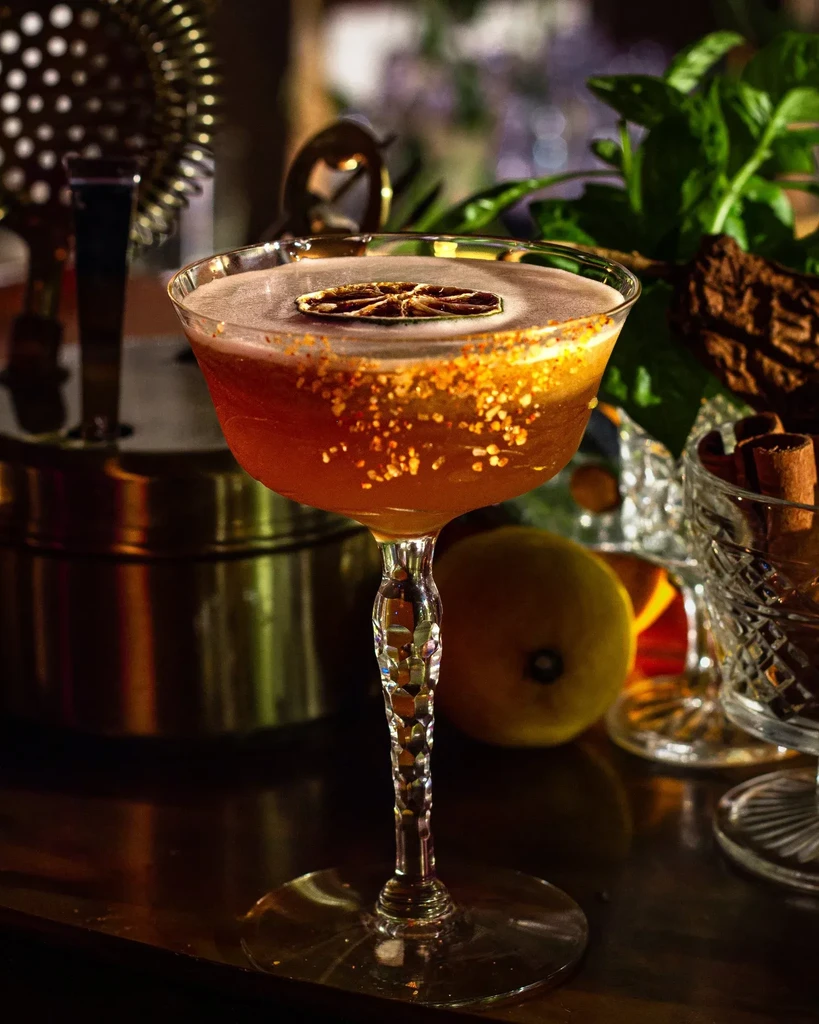 Frothy amber cocktail in coupe glass, with dried citrus and golden rim.