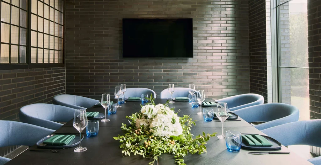 Modern dining room, long dark table, ten blue chairs, white flowers.