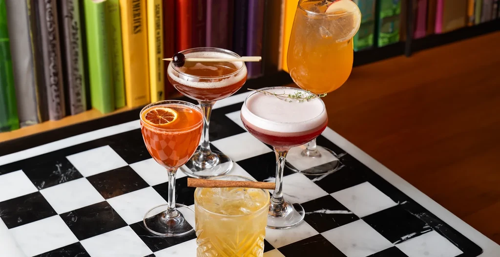 Five distinct garnished cocktails on a black and white checkered surface.