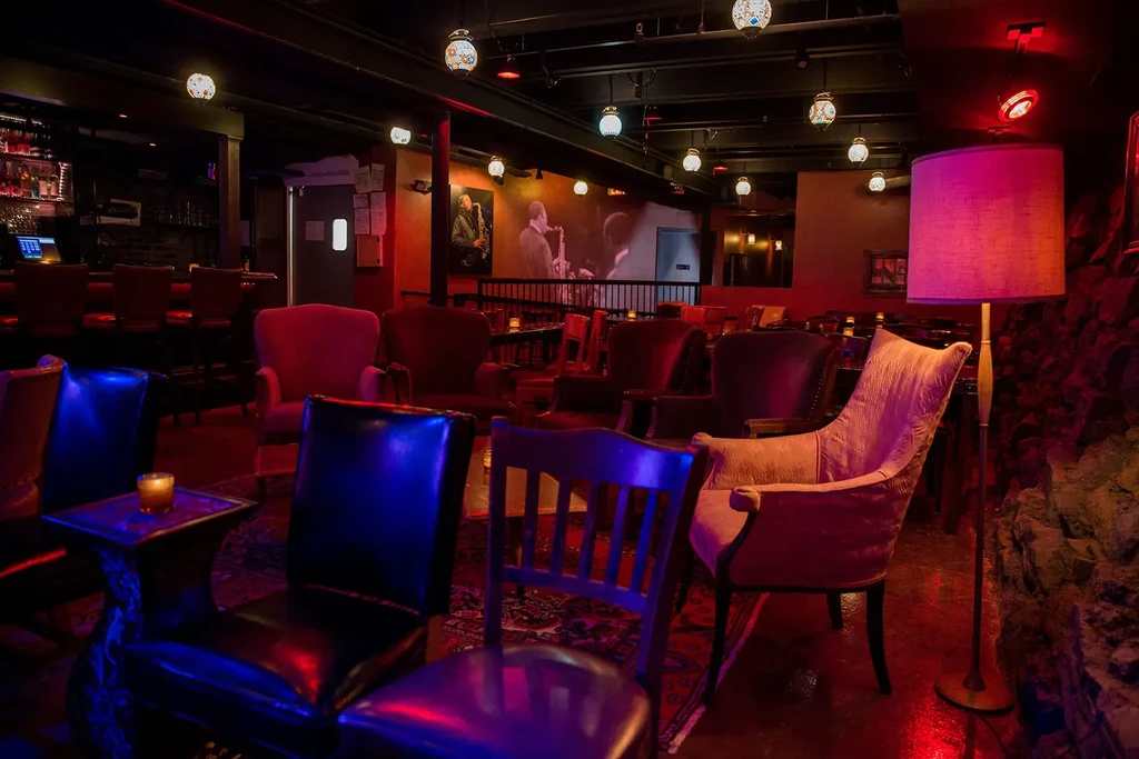 Dimly lit bar interior, red walls, plush seating, bar, and artwork.