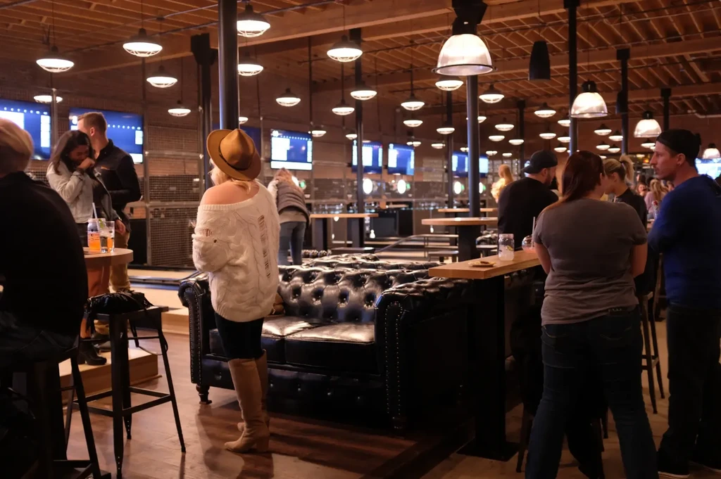 People socialize in a lively, modern-industrial restaurant interior.