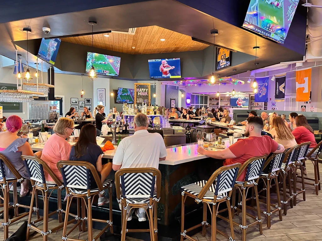 Lively sports bar interior with patrons at a well-lit bar and TVs.