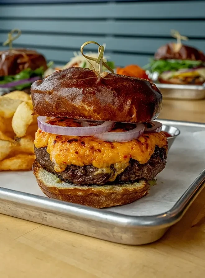 Gourmet burger with pretzel bun, melted cheese, red onion, and crinkle-cut fries.
