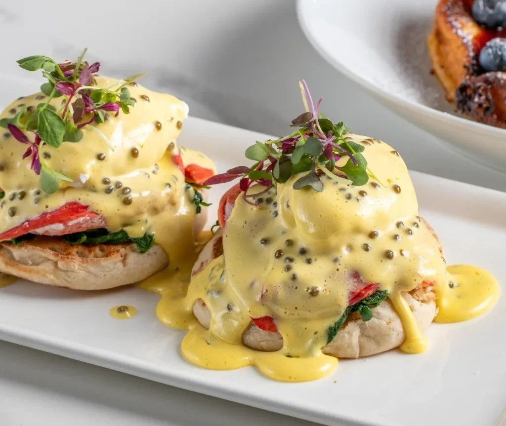 Two seafood Eggs Benedict with caviar, hollandaise, and microgreens.