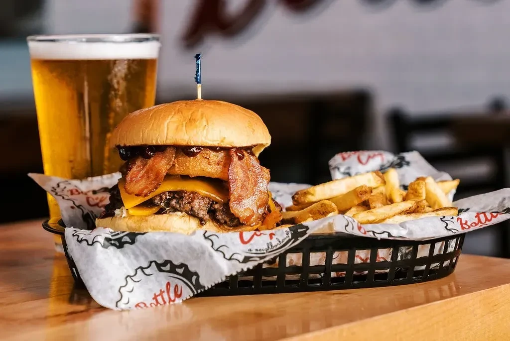 Gourmet burger, fries, and beer on a light wooden table.