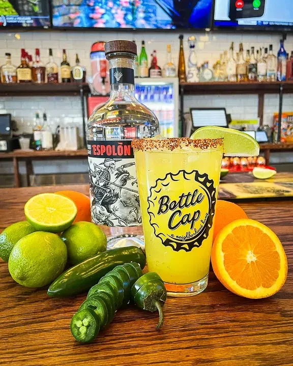 Espolòn tequila bottle, chili-salted cocktail, limes, jalapeños on a bar.
