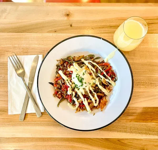 Overhead shot of breakfast hash topped with egg, sauce, chives, and juice.