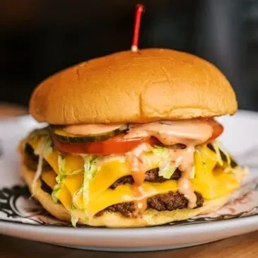 Double-patty burger with melted cheese, lettuce, tomato, pickles, creamy sauce.