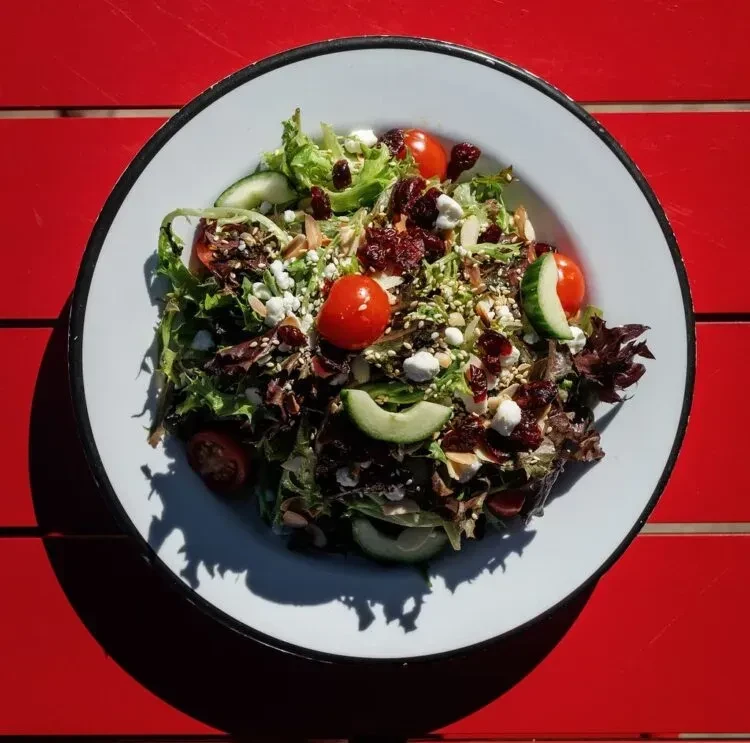 Colorful salad with greens, tomatoes, cheese, cranberries, and nuts on a red table.