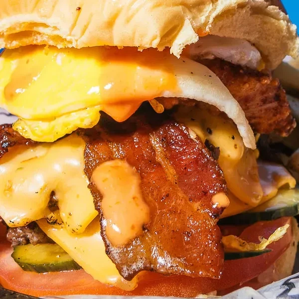 Gourmet burger with fried egg, bacon, melted cheese, patty, pickles, tomato.