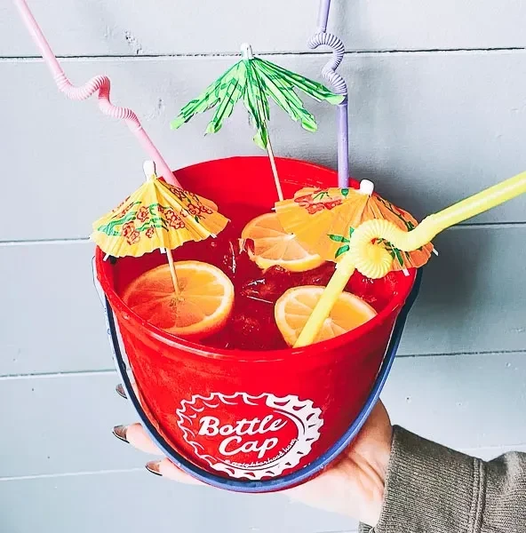 Large red drink bucket with beverage, ice, citrus, umbrellas, and straws.