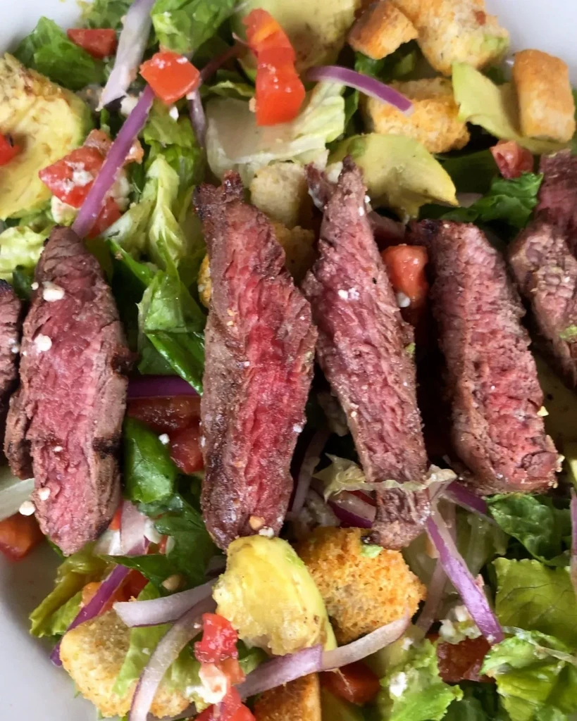 Close-up of medium-rare steak salad with lettuce, tomatoes, onions, and croutons.