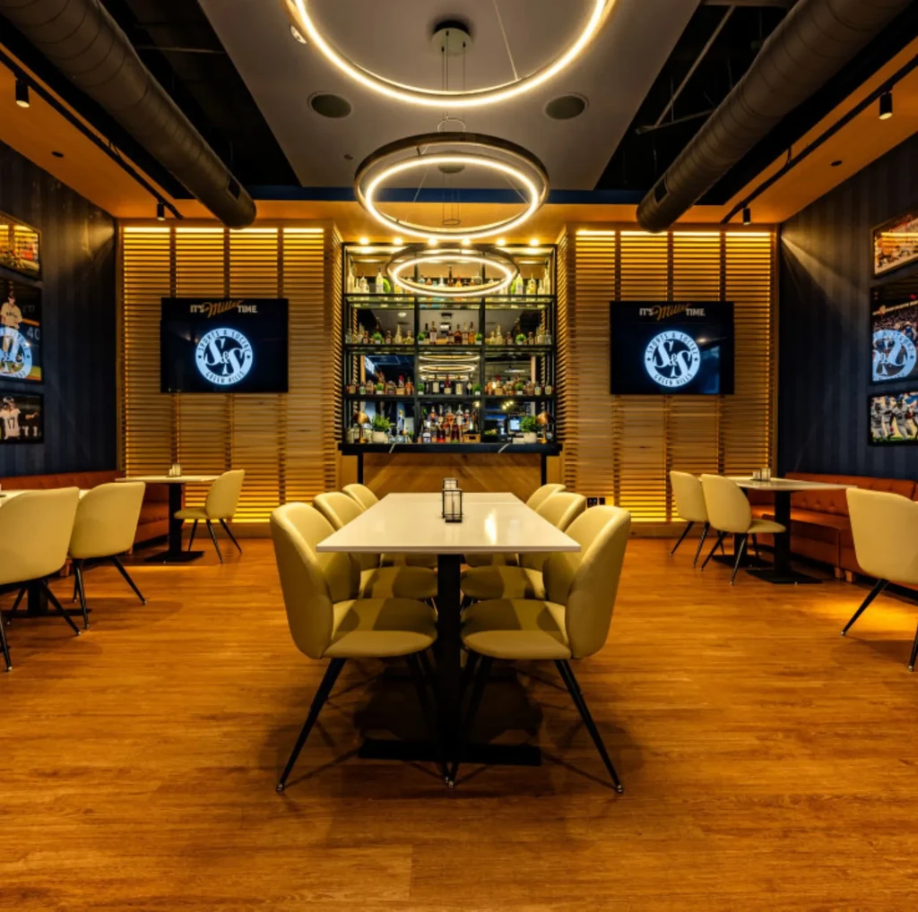 Modern restaurant interior with yellow chairs, lit bar, and sports decor.