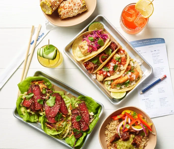 Overhead flat lay of Bartaco tacos, corn, lettuce wraps, rice, and beverages.