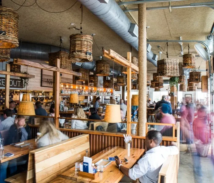 Bustling rustic-industrial restaurant with wicker lights, rope pillars, and bar.
