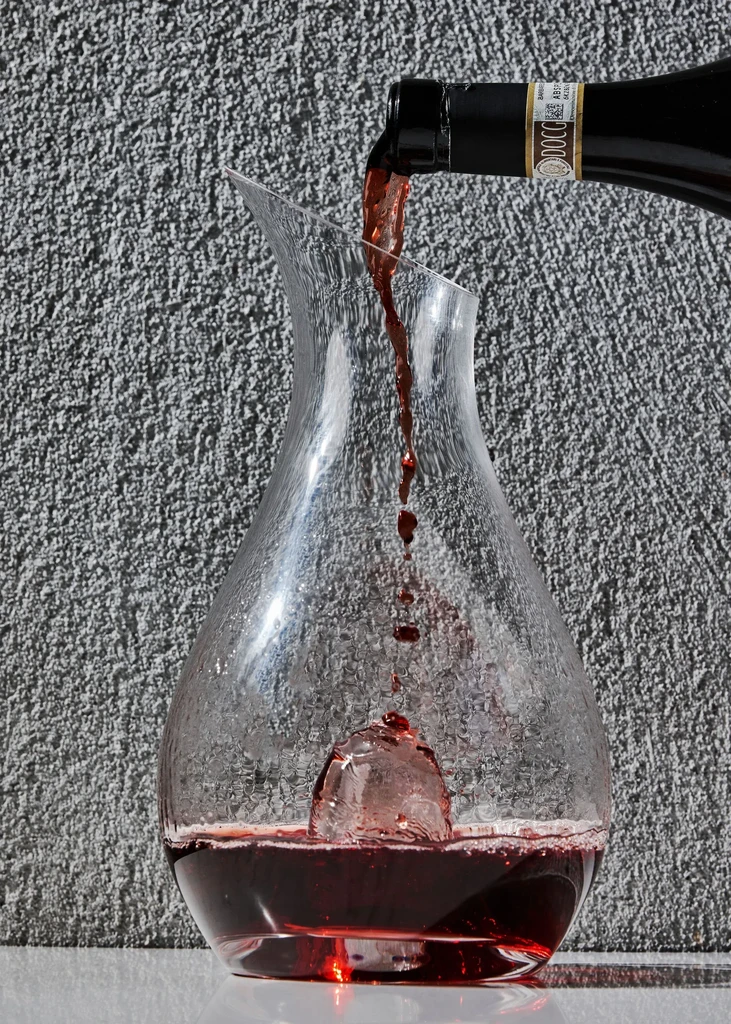 Red wine pouring from bottle into a decanter with ice.