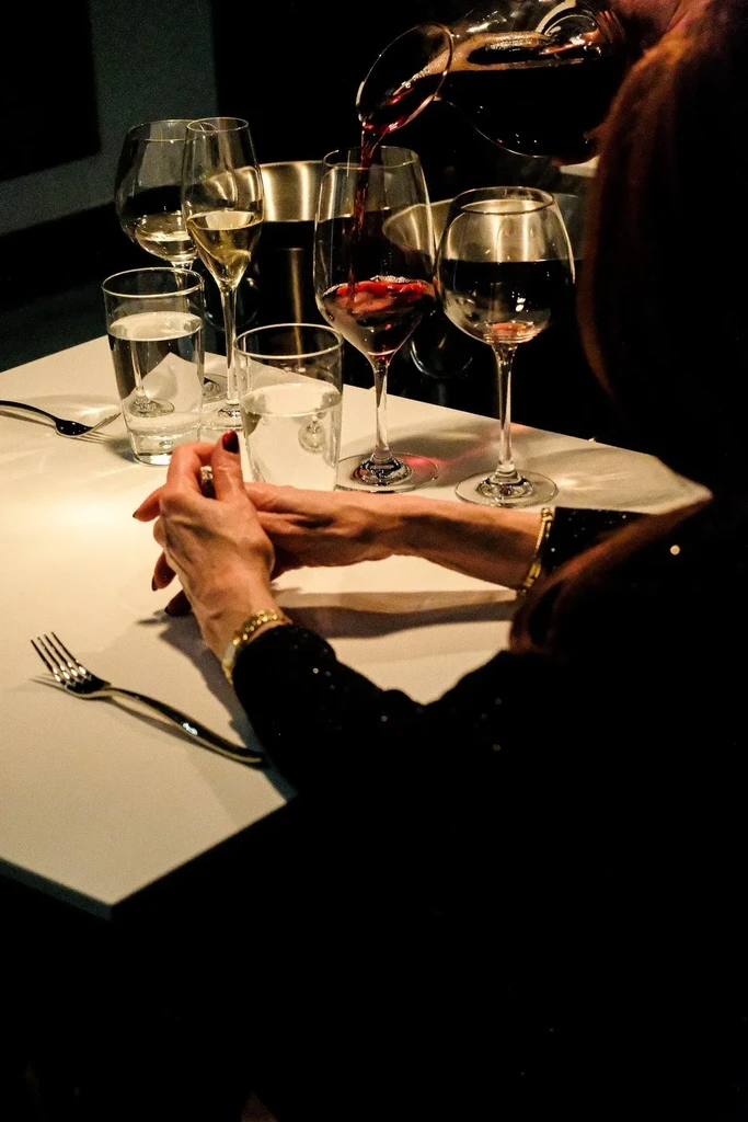 Red wine poured from decanter into glass on a dimly lit table.