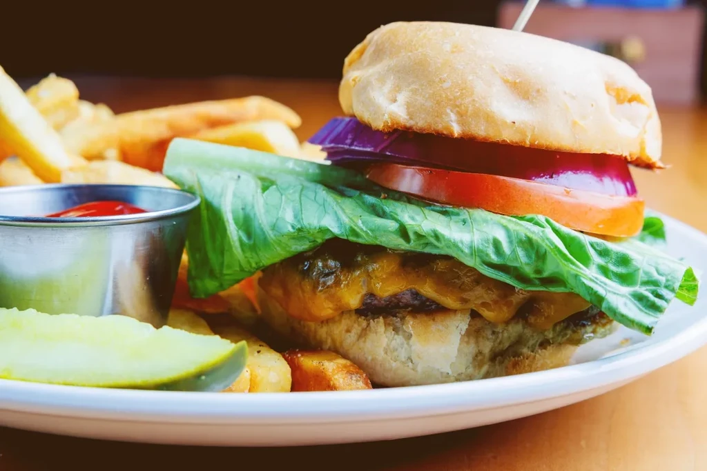 Gourmet cheeseburger, fries, ketchup, and pickle on a white plate.