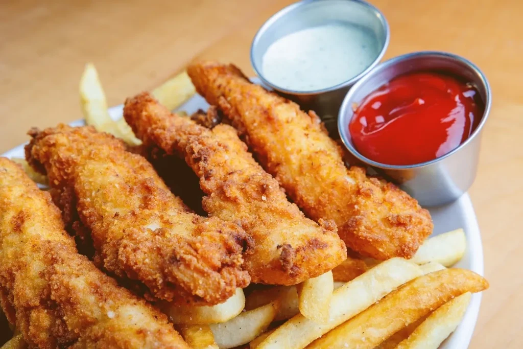 Plate of breaded food, french fries, ketchup, and a creamy dipping sauce.