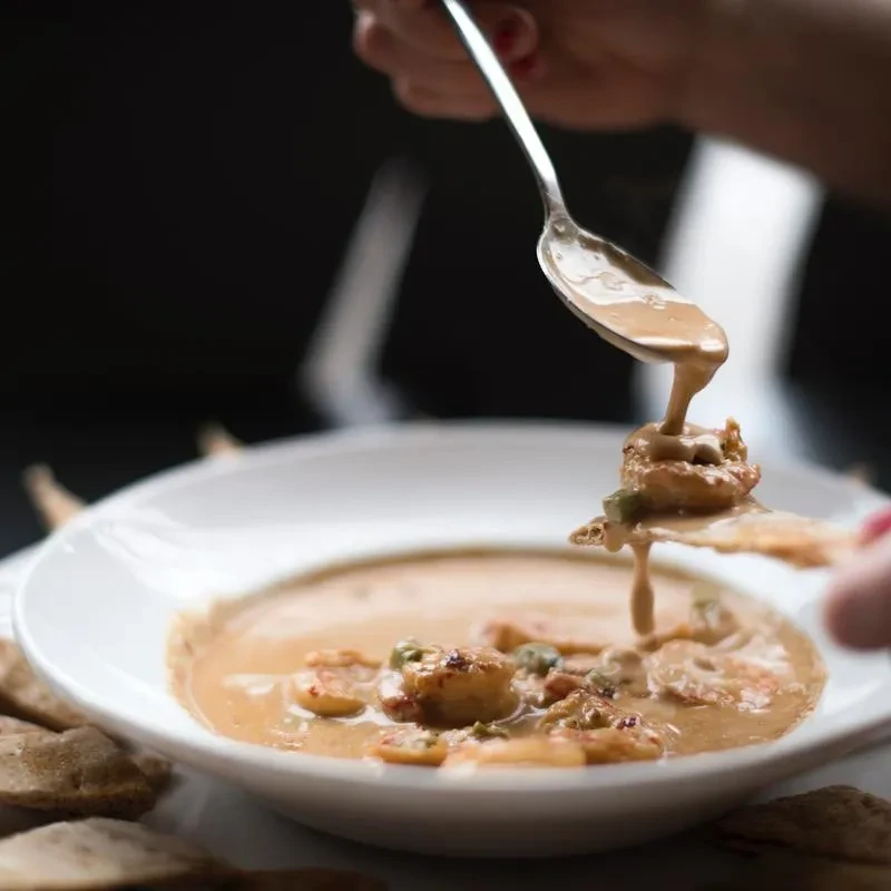 Hands scooping creamy shrimp stew with a spoon and cracker.
