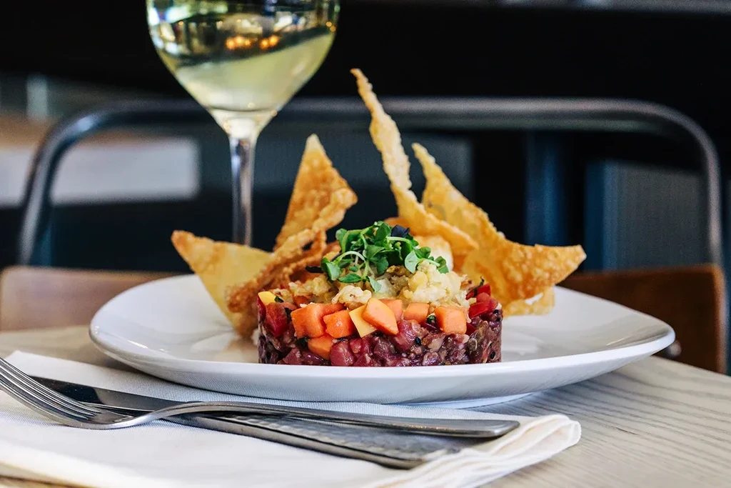 Cylindrical tartare with chips, microgreens, and white wine in a restaurant.